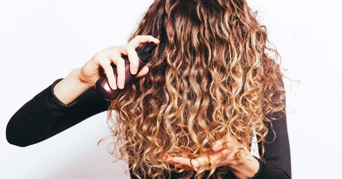 a woman with curly hair overher face and squirting serum into it
