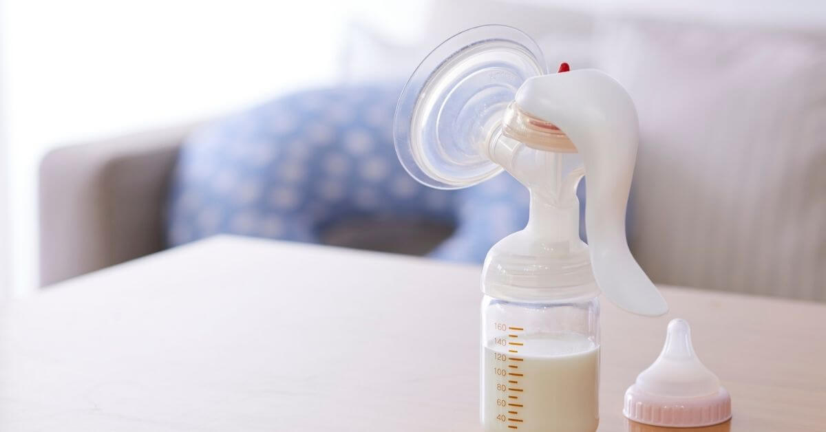Manual breast pump with milk-filled collection bottle resting on a table in a calm home setting.