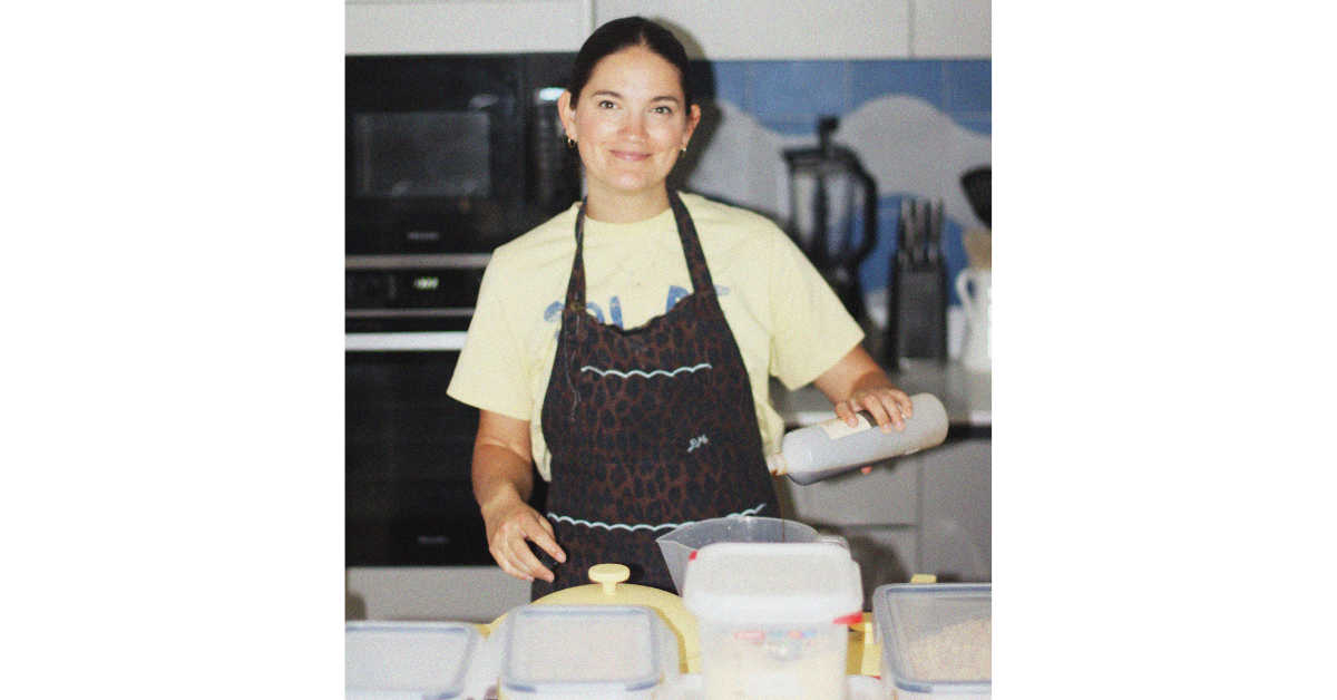 Mel, a doula and founder of Milk It, standing in her kitchen wearing an apron and preparing lactation cookies on a countertop.