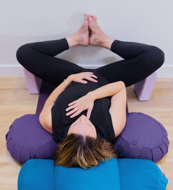 A woman lying on her back on a yoga bolser with her legs in an open position at yoga