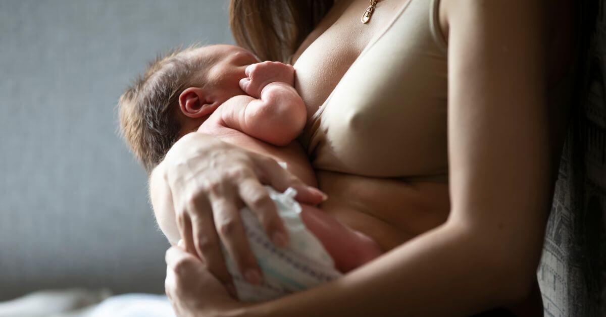 Woman wearing beige bra holding baby as she breastfeeds